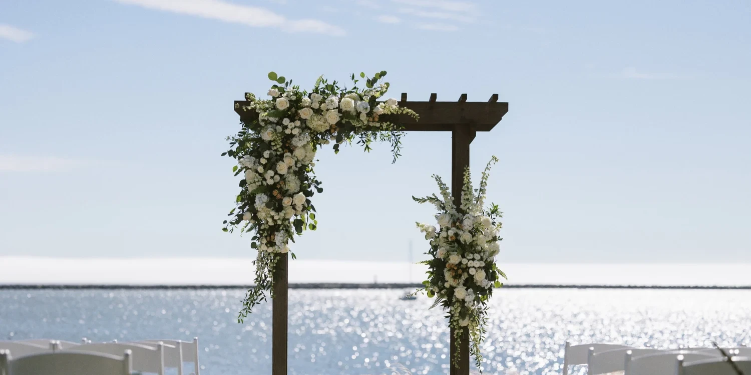 Wedding arch with white and green florals on the beach at Half Moon Bay